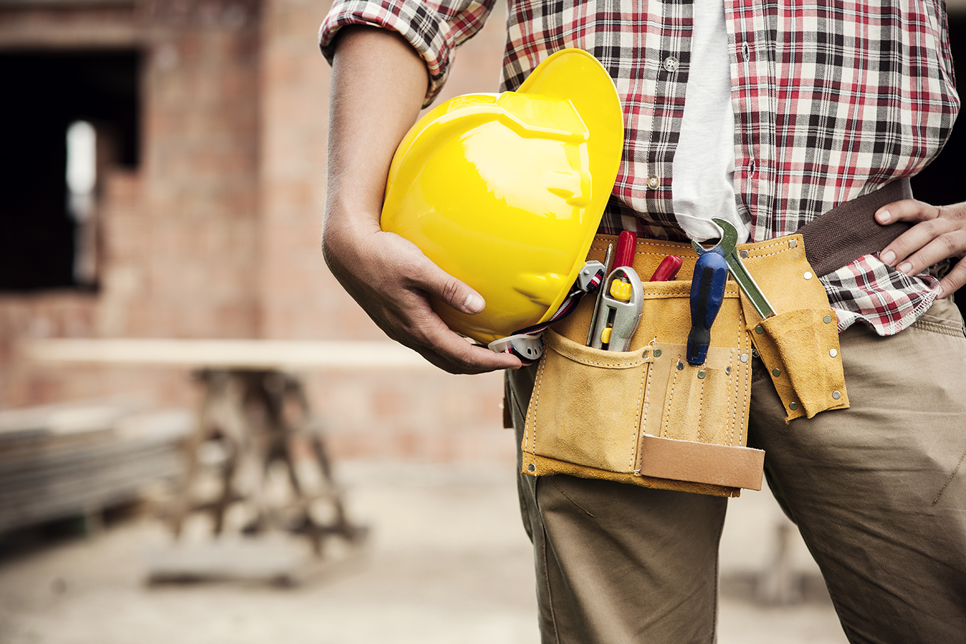 a construction worker holding a yellow hard hat while wearing a tool belt