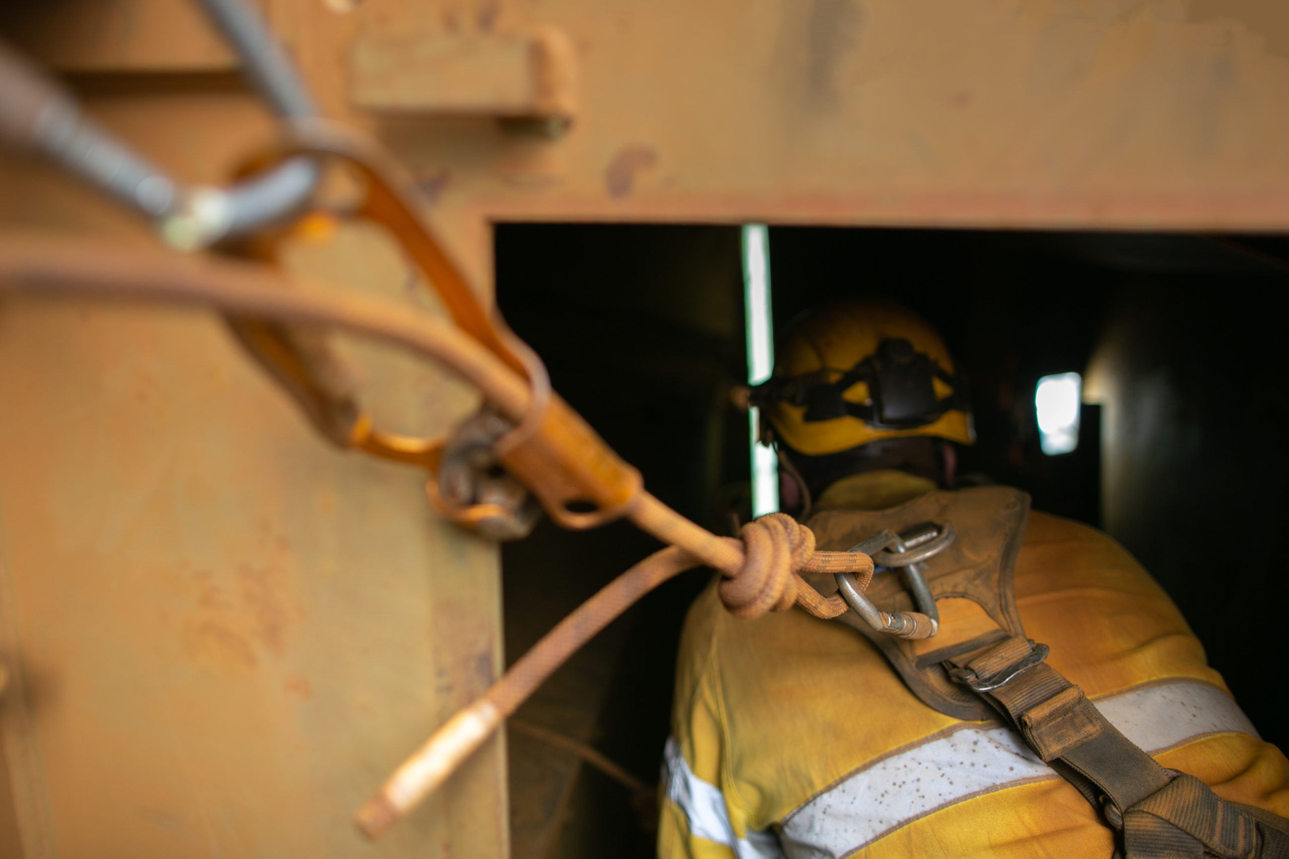 Close up shot of rope access worker wearing safety harness, helmet connecting three two one rescue pulley system into back of his safety harness loop prior entering working inside confined space